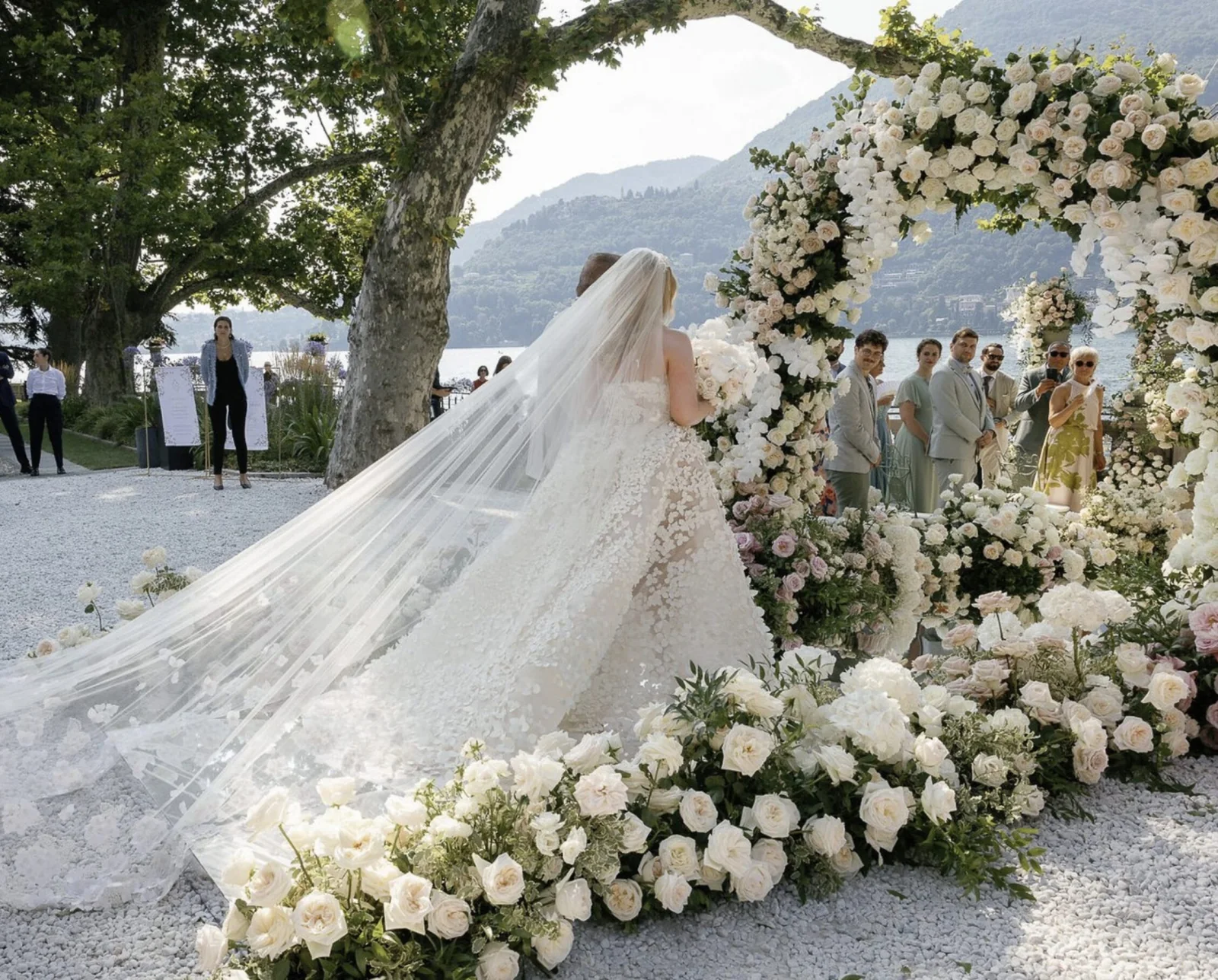 Bride walking beneath a floral arch beside a lake